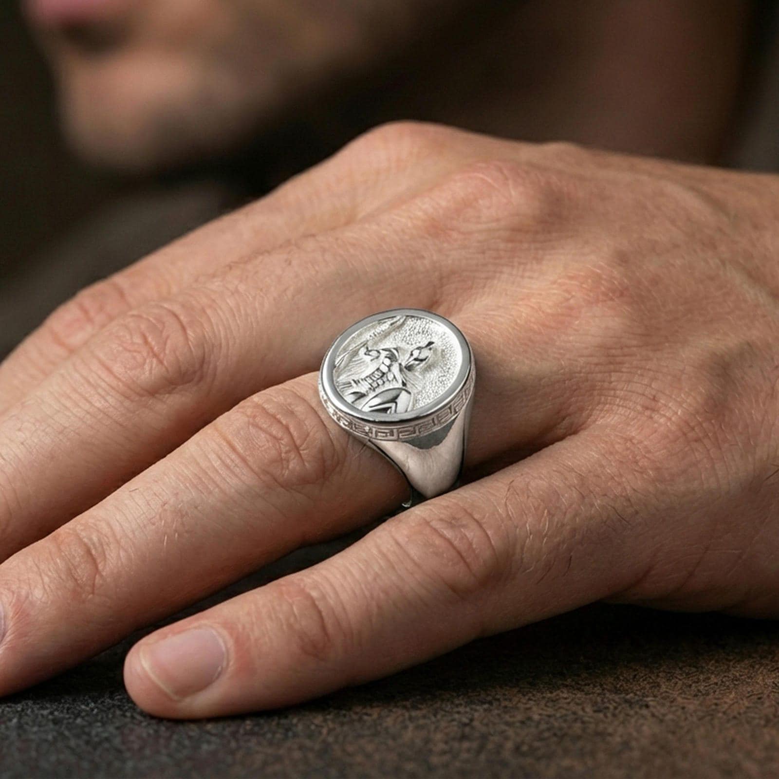 Polished silver Greek soldier signet ring worn on the finger, wearable photo highlighting reflective metal and engraved warrior scene