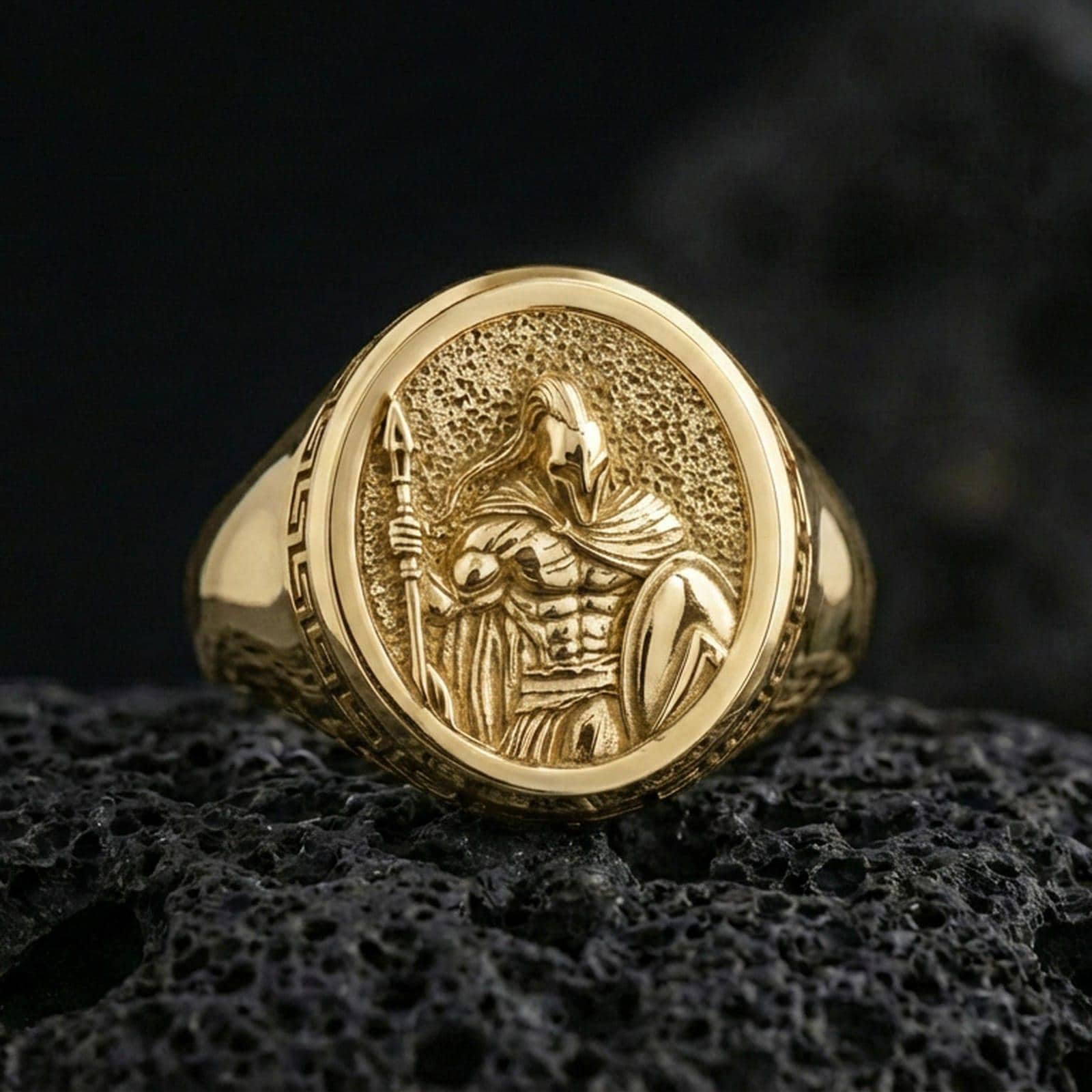 Gold plated Spartan soldier signet ring with spear-and-shield design and Greek key side detail, product photo on porous volcanic rock