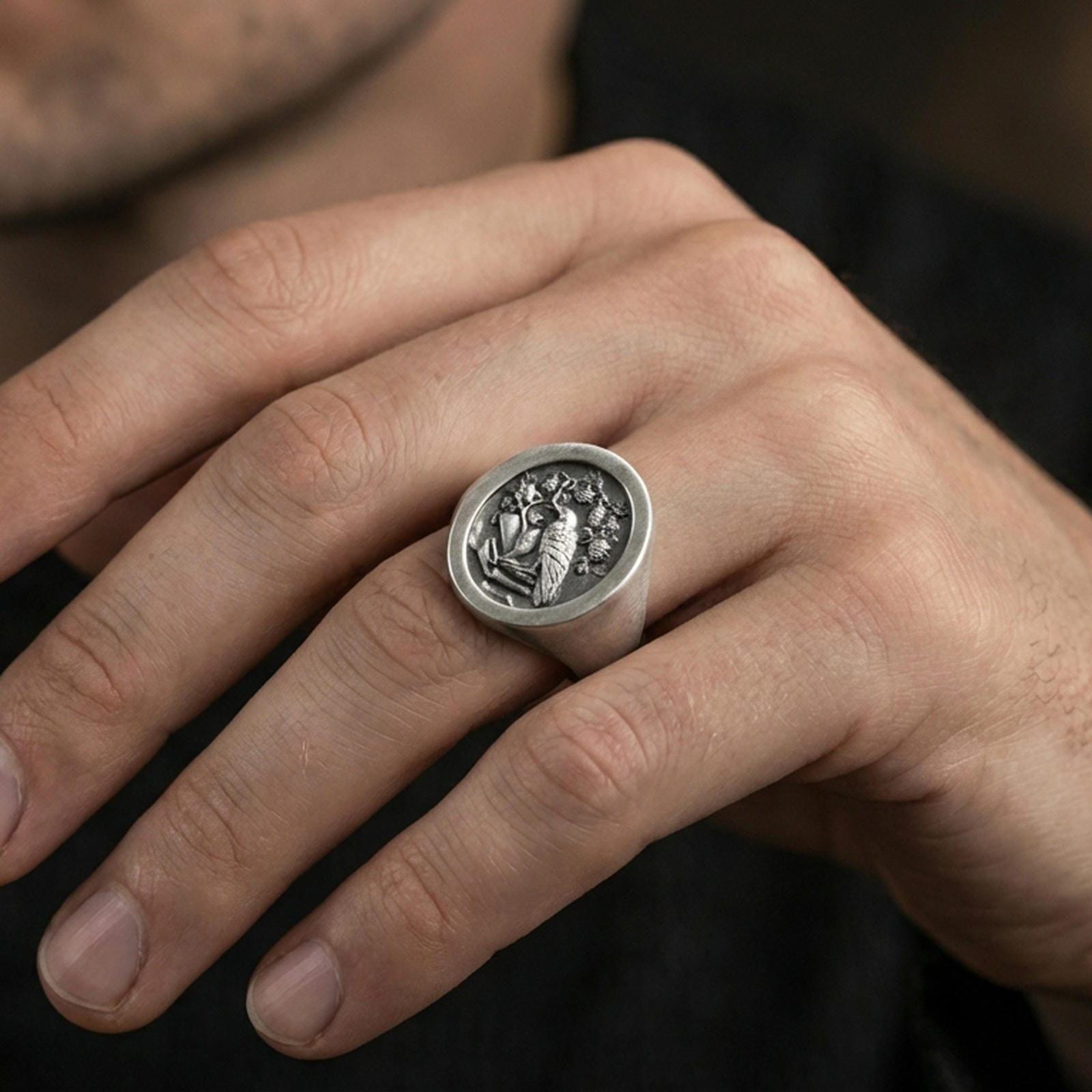 Oxidized raven signet ring worn on a finger, close-up lifestyle photo highlighting the engraved crest and dark antique depth
