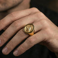 Load image into Gallery viewer, Gold plated raven signet ring worn on a finger, lifestyle image focusing on the bold emblem face and raised engraving
