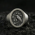 Load image into Gallery viewer, Oxidized sterling silver signet ring with raven and botanical crest engraving, macro product photo on black volcanic rock

