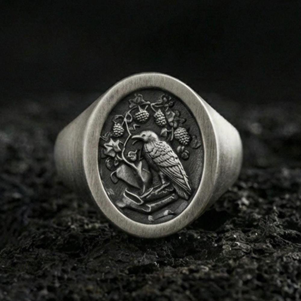 Oxidized sterling silver signet ring with raven and botanical crest engraving, macro product photo on black volcanic rock