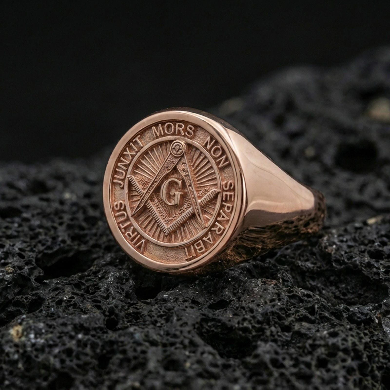 Rose gold plated Freemason signet ring with engraved square and compass emblem and motto ring border, macro image on volcanic rock