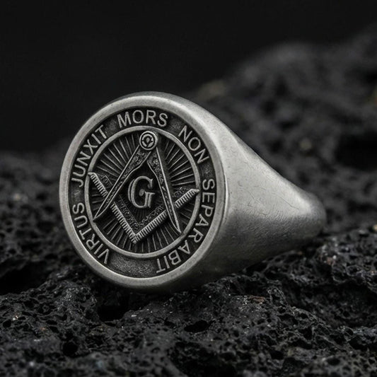 Oxidized sterling silver Masonic signet ring with square and compass “G” emblem and Latin motto, macro photo on black volcanic rock