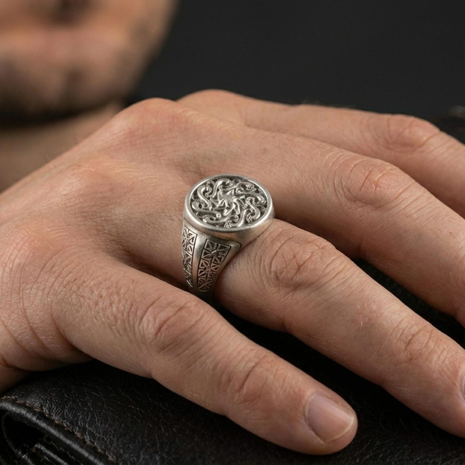Oxidized spiral sun signet ring worn on a finger, close-up lifestyle photo highlighting the swirling relief and textured background