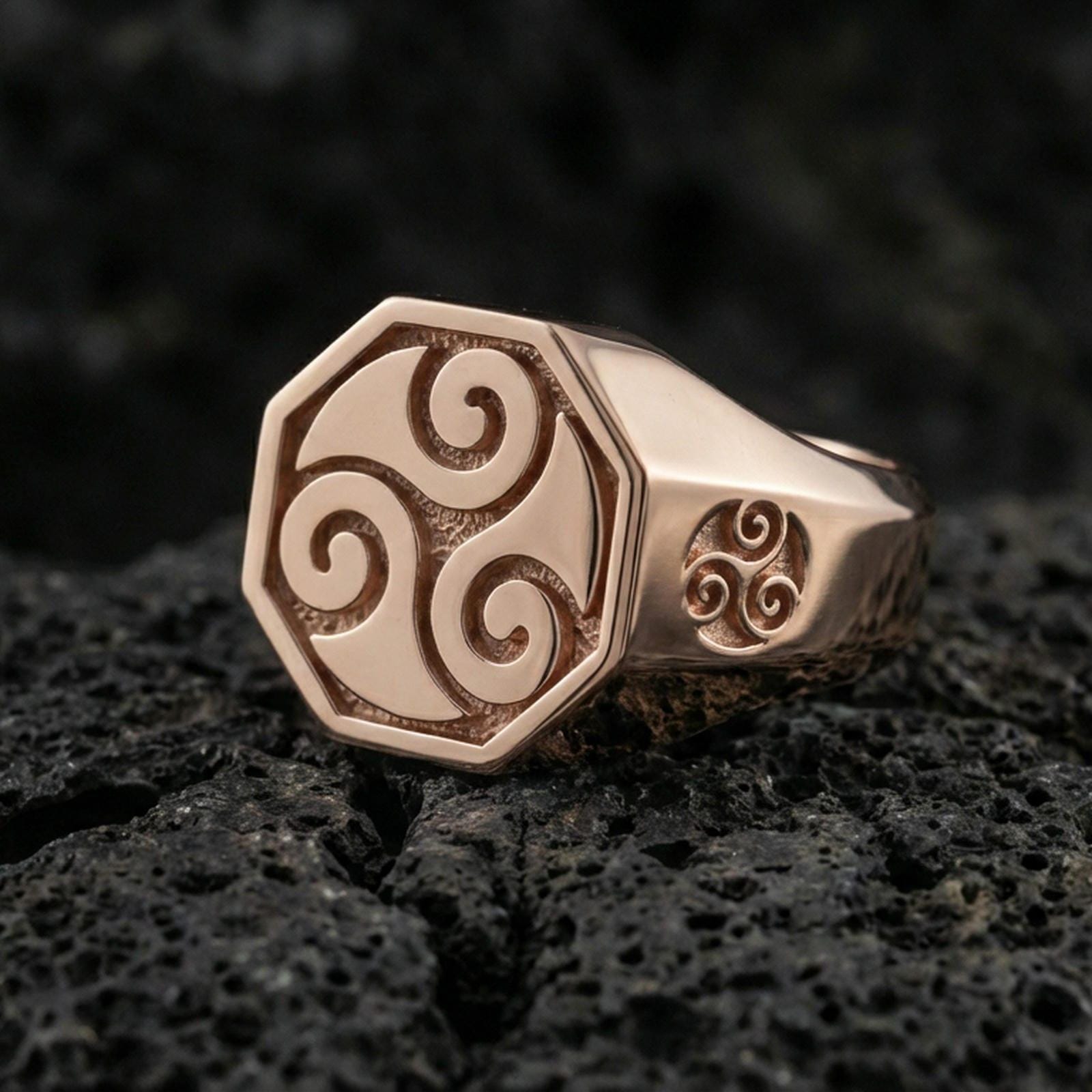 Rose gold plated octagonal signet ring with Celtic triskelion swirl design and side symbol detail, product-only macro shot on volcanic rock