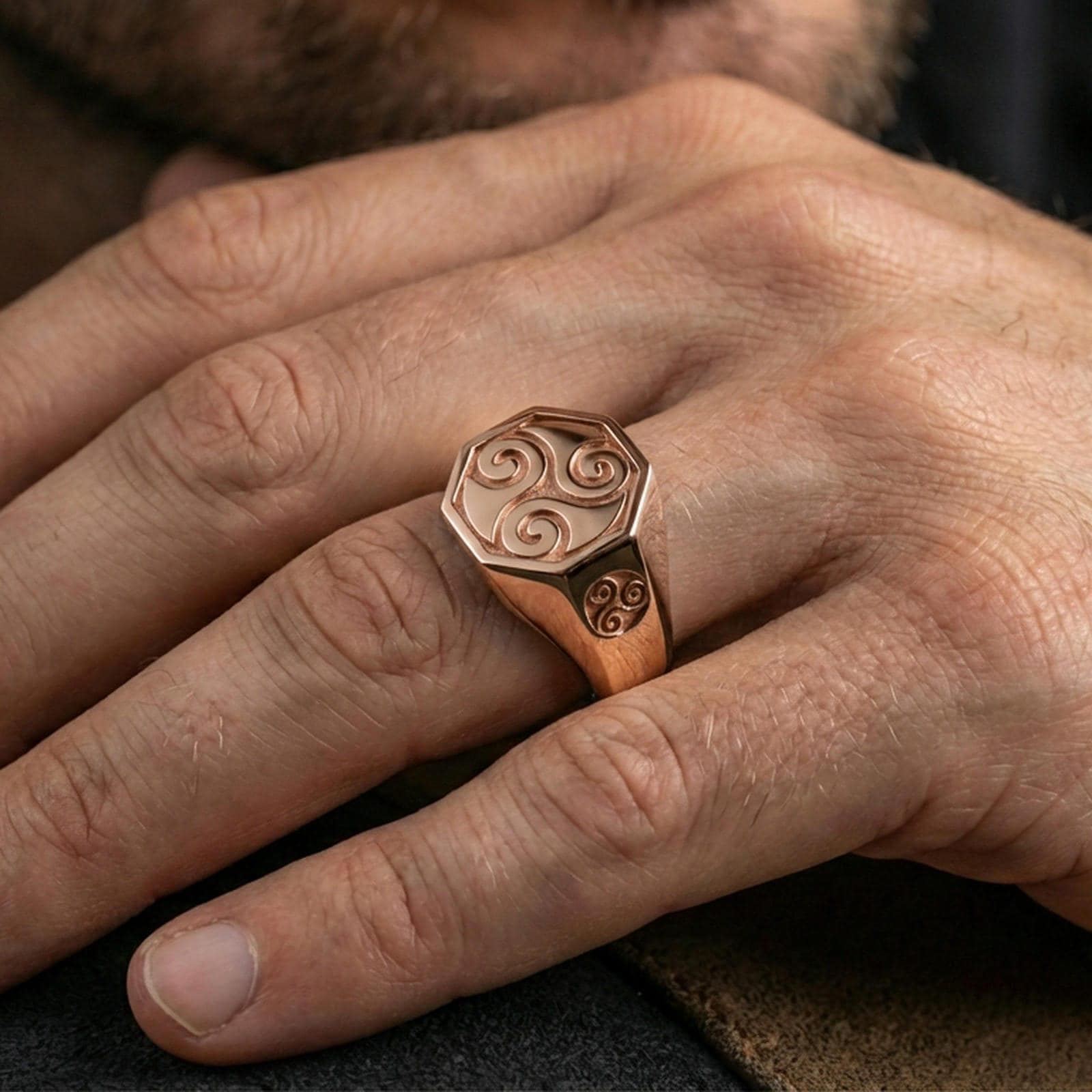Rose gold plated triskelion signet ring worn on a finger, close-up lifestyle photo showcasing the octagonal signet profile and swirl motif