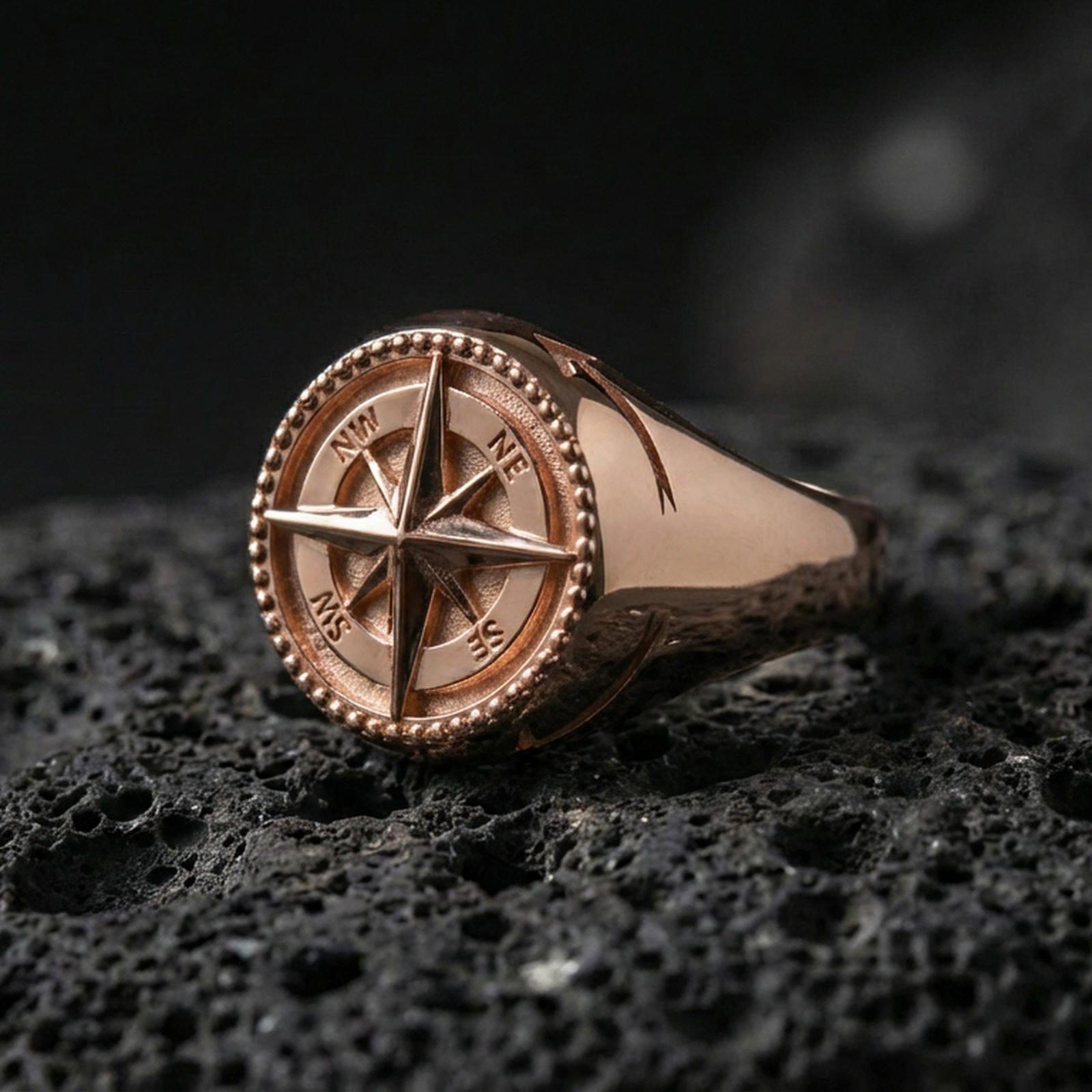 Rose gold plated compass signet ring with 3D wind rose star, direction markings, and beaded rim, product-only macro shot on volcanic rock