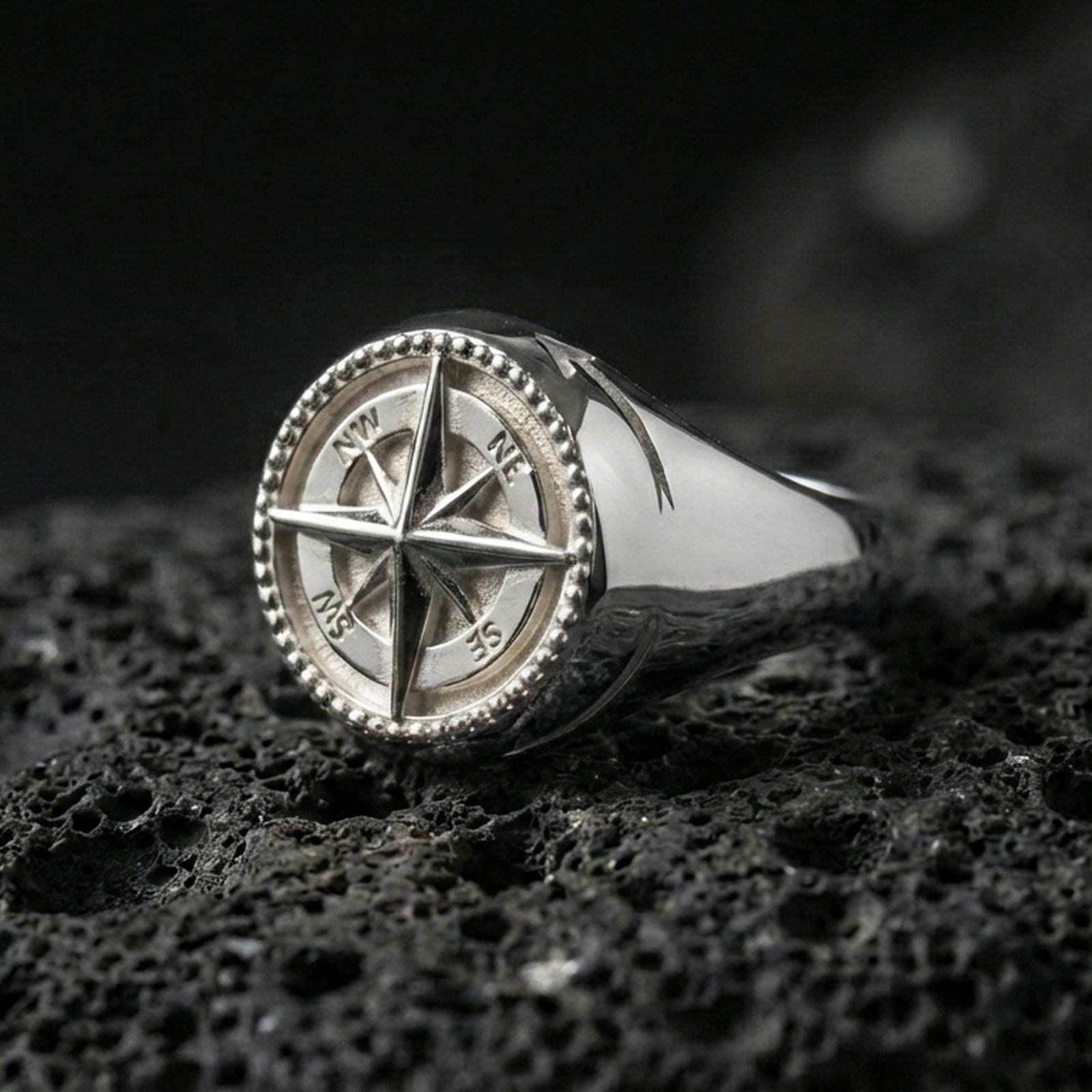 Polished silver compass signet ring featuring a 3D wind rose star and beaded border edge, close-up product shot on volcanic stone