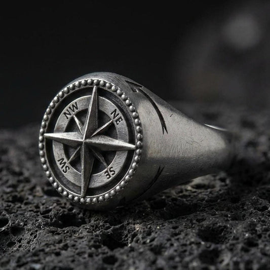 Oxidized sterling silver compass signet ring with raised wind-rose star and NW NE SW SE lettering, macro photo on black volcanic rock