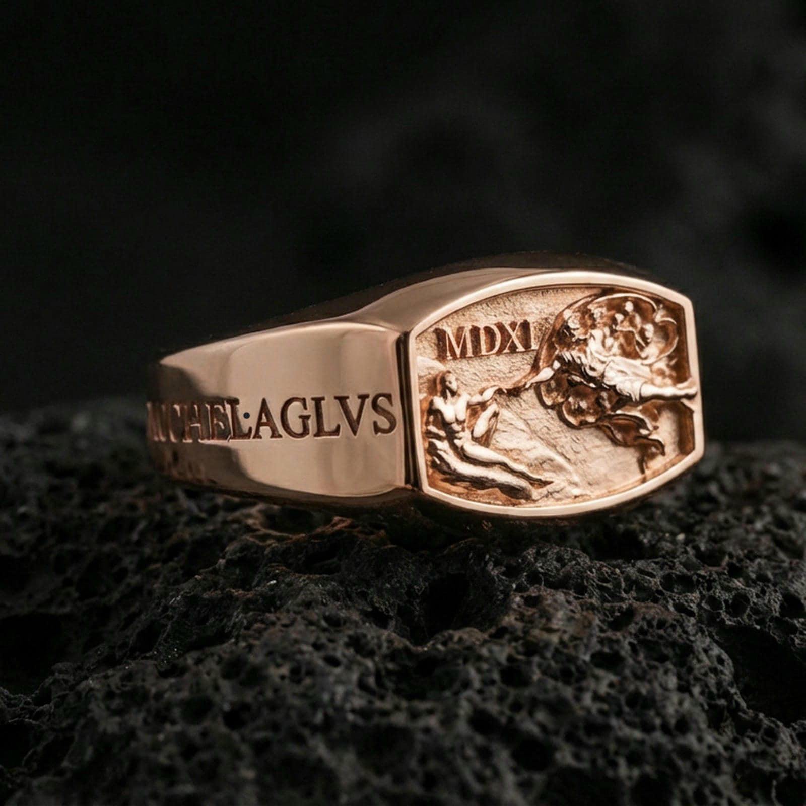 Rose gold plated Saint Michael ring with engraved lettering and sculpted battle tableau on the face, close-up photo on volcanic rock