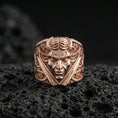 Load image into Gallery viewer, Rose gold plated demon face signet ring with crossed blades and decorative patterning, close-up photo on volcanic rock
