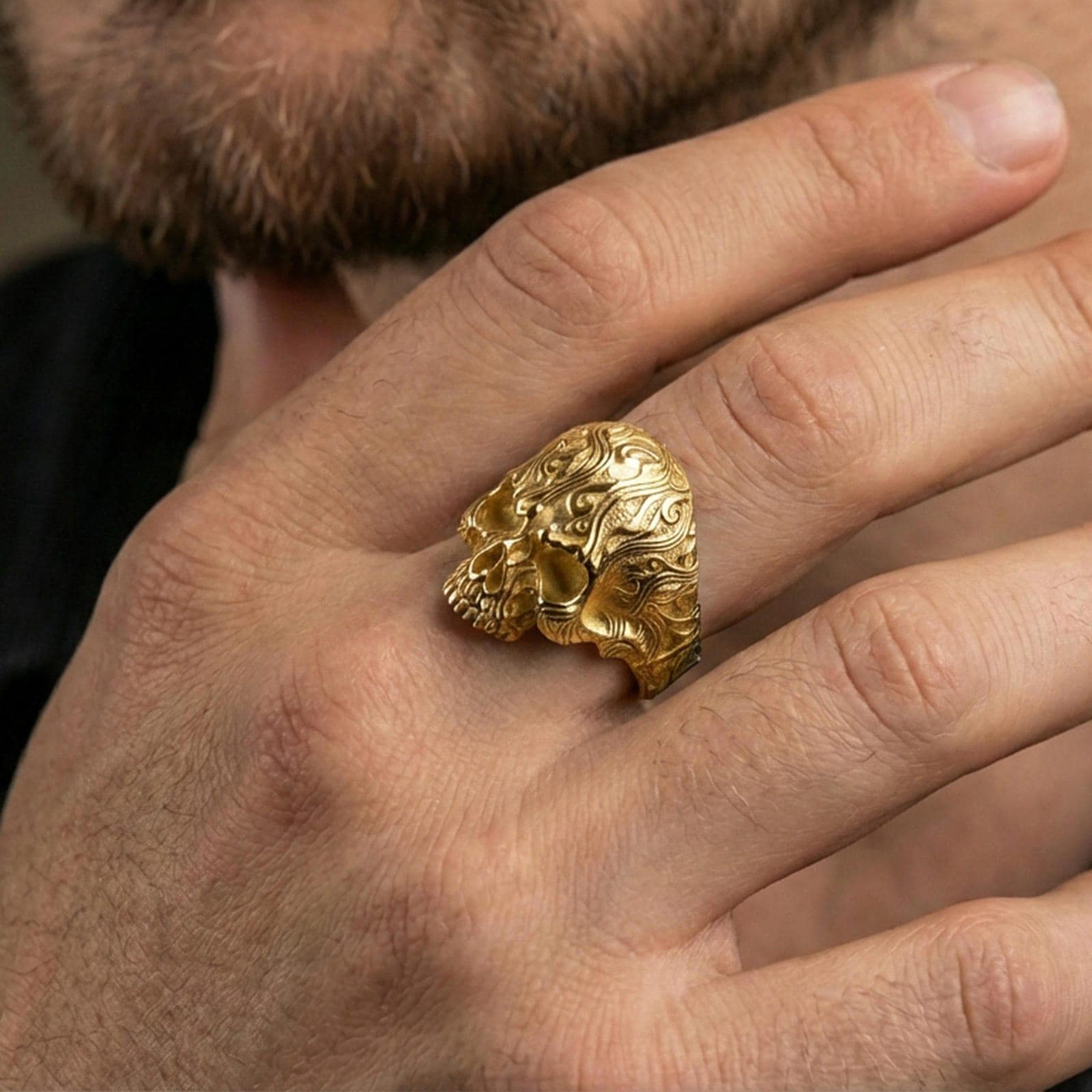 Gold plated skull ring worn on a finger, close-up lifestyle image highlighting the detailed scrollwork and high-relief skull face