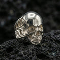 Load image into Gallery viewer, Polished silver skull ring featuring clean sculpted cranium and defined teeth detail, close-up product shot on volcanic stone
