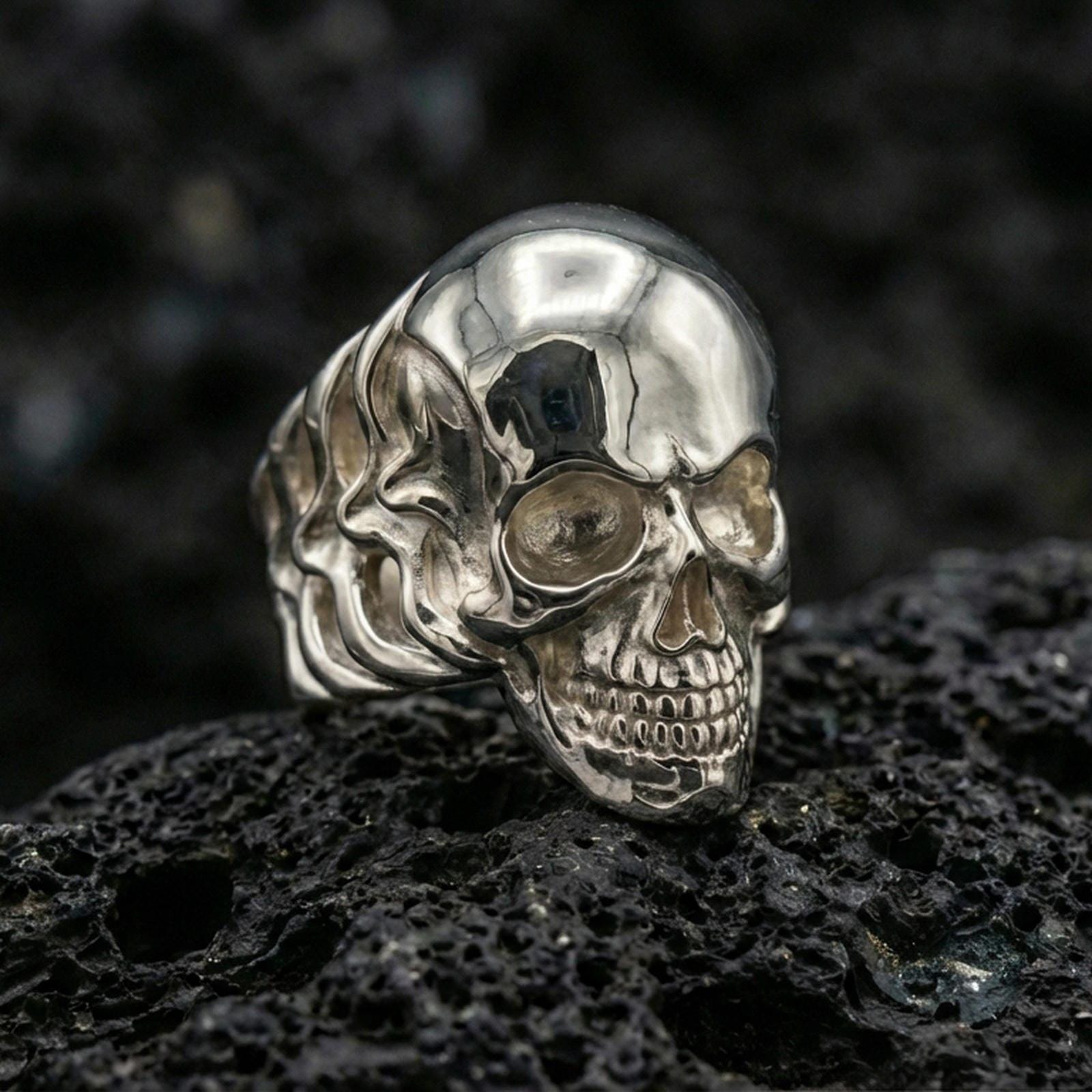 Polished silver skull ring featuring clean sculpted cranium and defined teeth detail, close-up product shot on volcanic stone