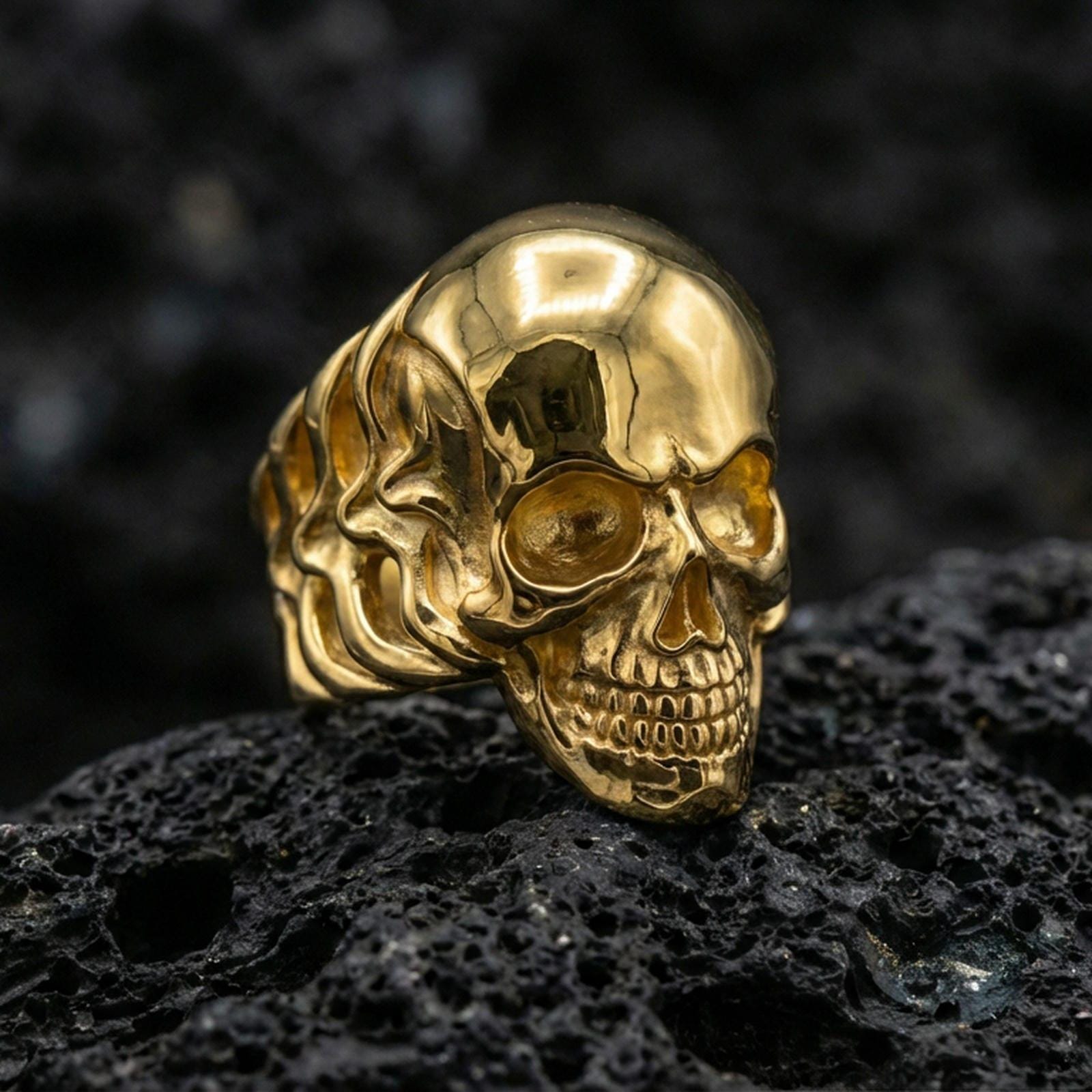 Rose gold plated skull ring with sleek rounded skull design and shadowed eye cavity detail, close-up on volcanic rock