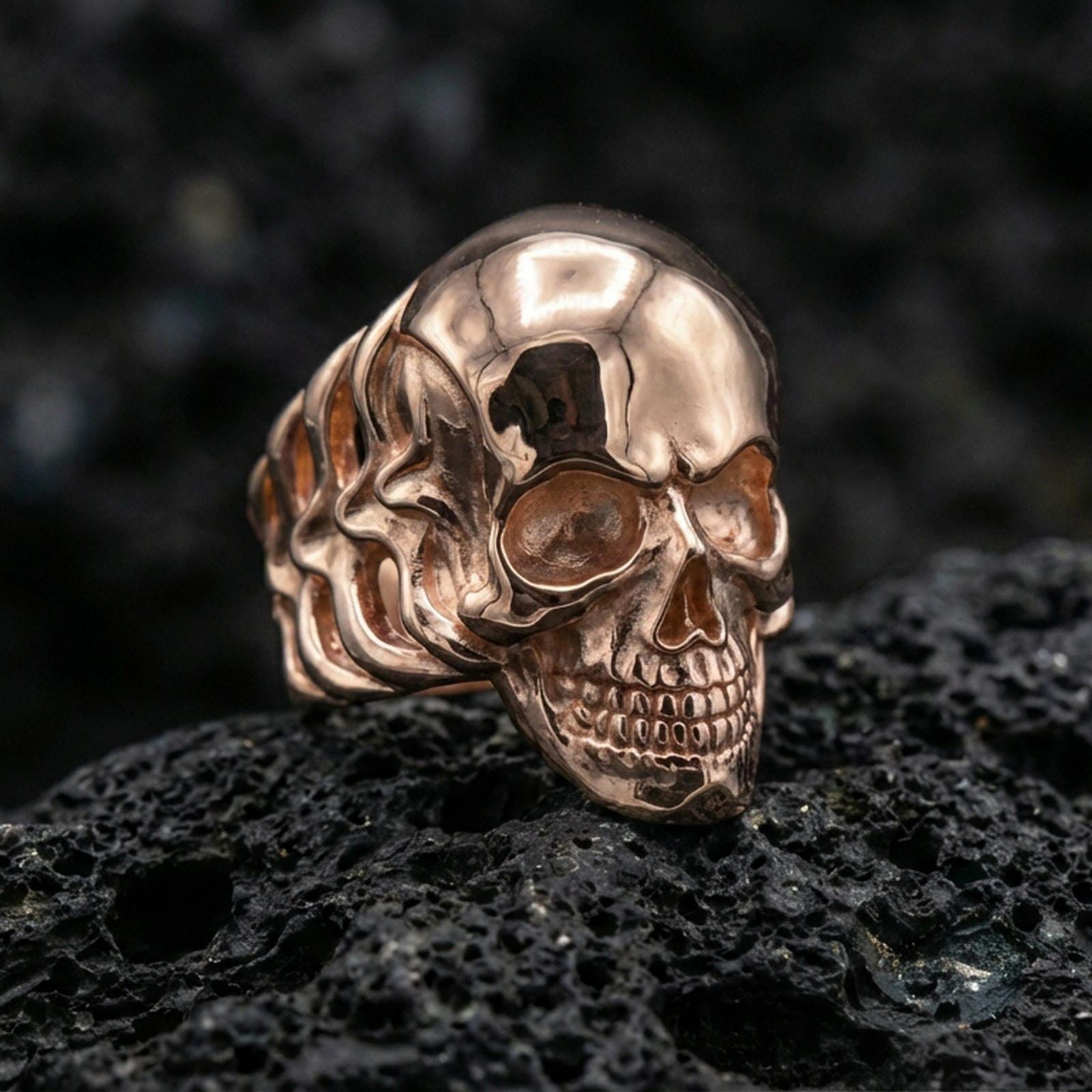 Gold plated skull ring with minimalist smooth head finish and high-relief jawline carving, product-only macro image on black volcanic rock