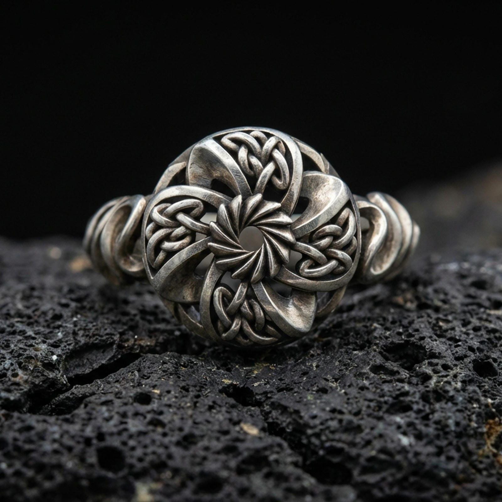 Oxidized sterling silver Celtic windflower ring with openwork floral rosette and interlaced knot details, macro product photo on black volcanic rock