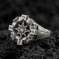 Load image into Gallery viewer, Oxidized sterling silver compass ring with raised eight-point star and cardinal direction markers, macro product photo on black volcanic rock
