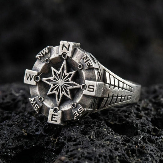Oxidized sterling silver compass ring with raised eight-point star and cardinal direction markers, macro product photo on black volcanic rock
