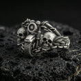 Load image into Gallery viewer, Oxidized sterling silver double skull motorcycle ring with detailed handlebars and chain links, macro product photo on black volcanic rock
