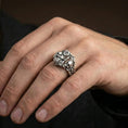 Load image into Gallery viewer, Polished silver biker skull ring on the finger, wearable photo emphasizing the dual skull detail and sculpted handlebar centerpiece
