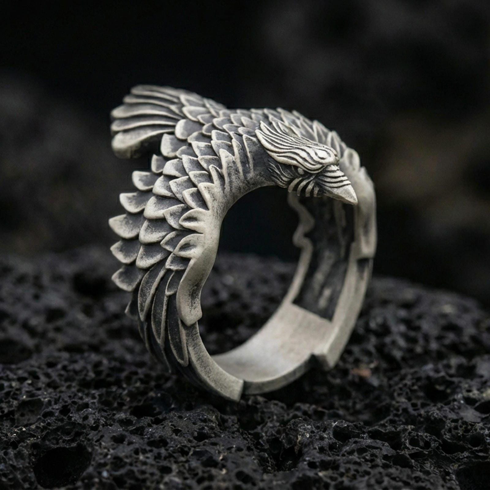 Oxidized sterling silver eagle wing open ring with layered feather texture and sculpted bird head, macro product photo on black volcanic rock