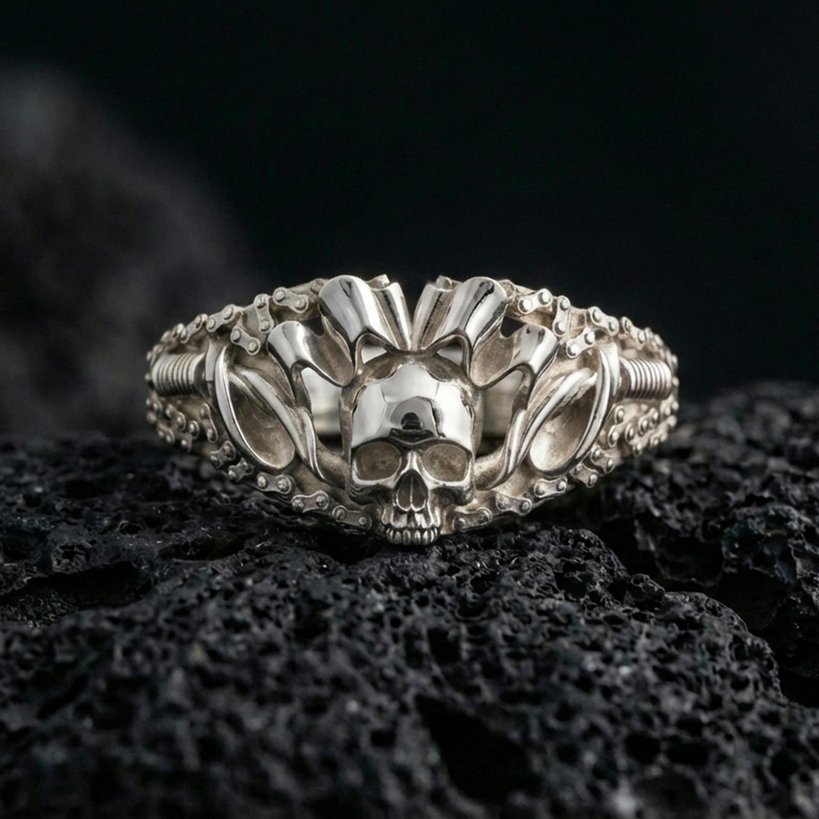 Polished silver skull ring featuring raised spiked crest and industrial chain textures on the band, close-up on volcanic stone