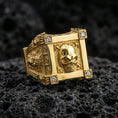 Load image into Gallery viewer, Gold plated skull ring with framed skull face and lab diamond accents on the corners, product-only macro image on volcanic rock
