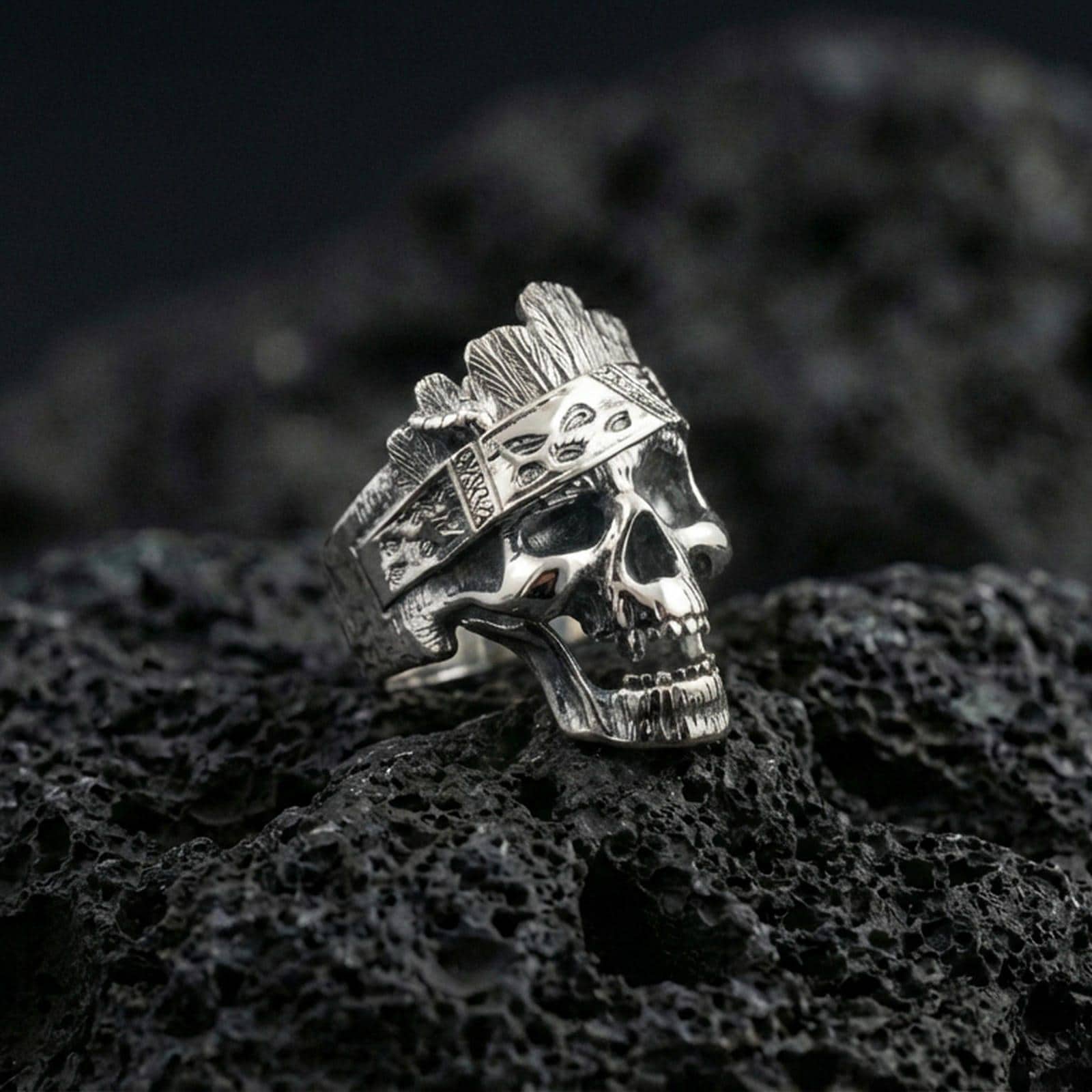 Polished silver skull ring featuring a wood bark texture finish and engraved side panels, close-up on volcanic stone