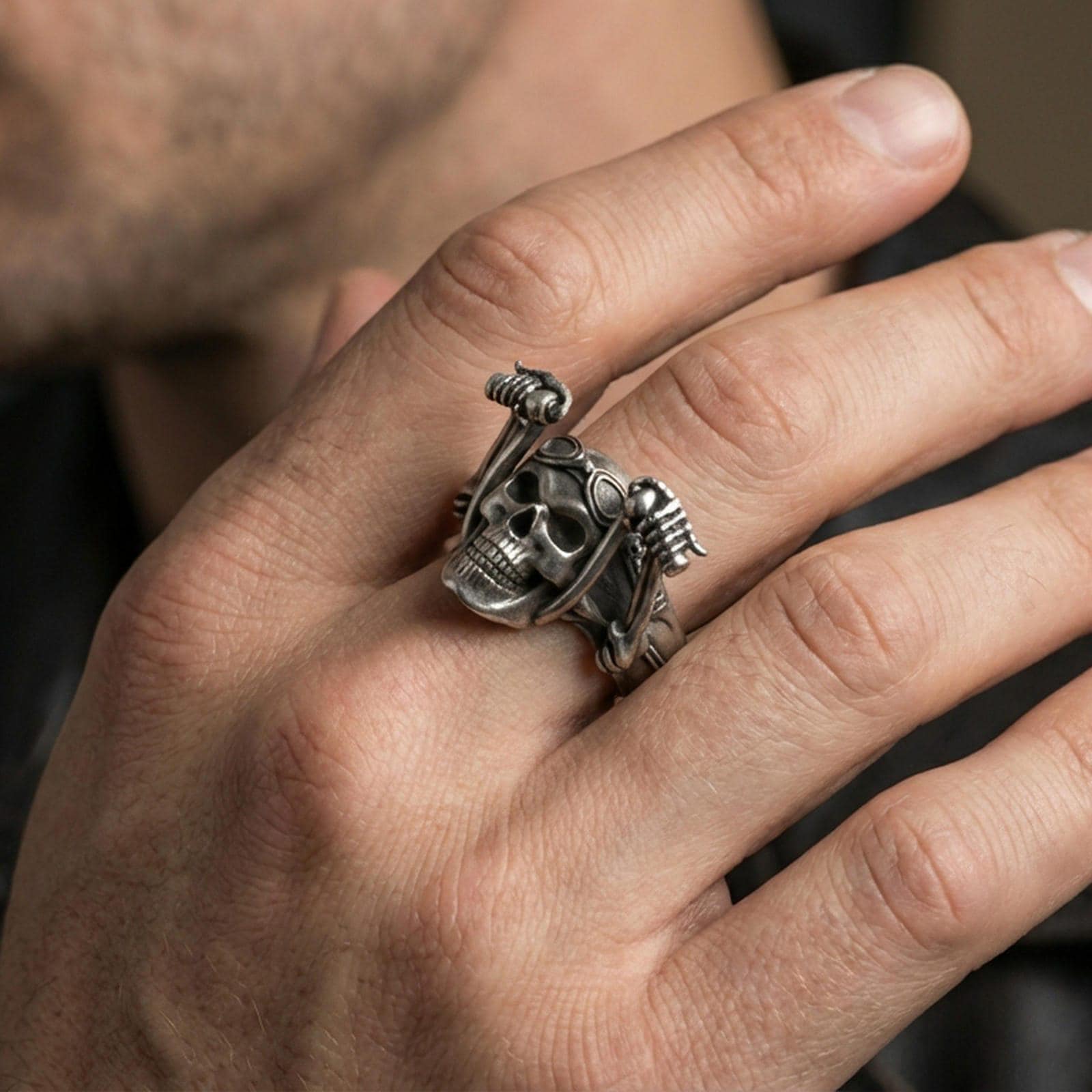 Oxidized biker skull ring worn on a finger, lifestyle close-up highlighting aviator goggles and skeleton hand details