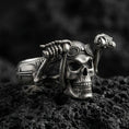 Load image into Gallery viewer, Oxidized sterling silver biker skull ring with aviator goggles and raised skeletal hands, macro product photo on black volcanic rock
