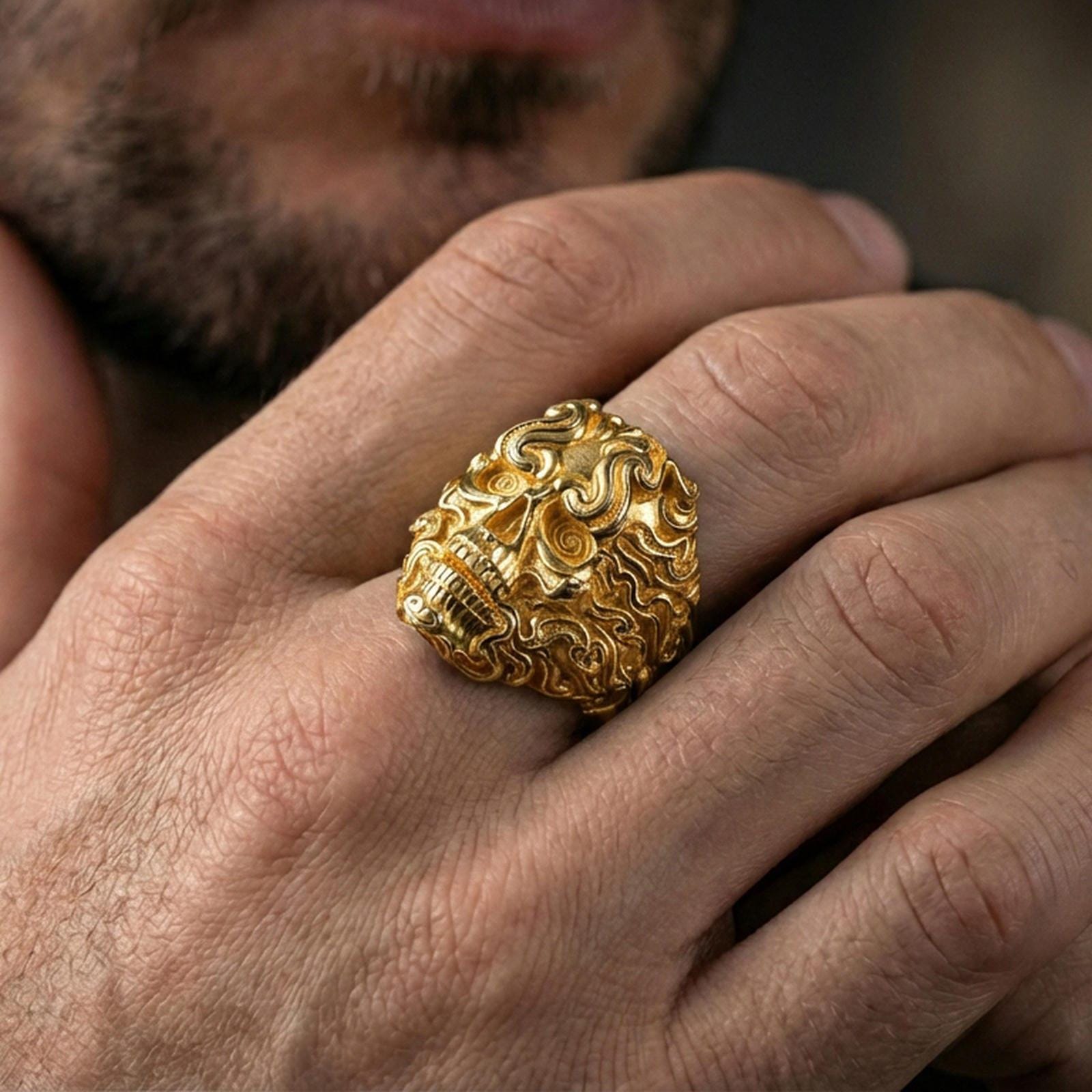 Gold plated smoke skull ring worn on a finger, close-up lifestyle image emphasizing the flowing curls and bold skull design
