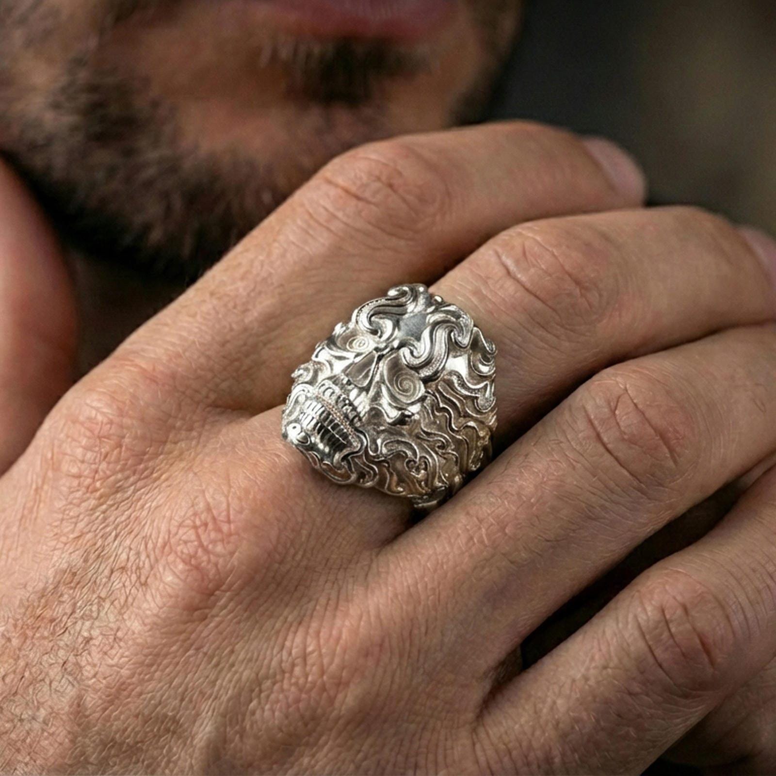 Polished silver ornate skull ring on the finger, wearable close-up focusing on spiral eyes and sculpted smoke details