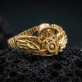 Load image into Gallery viewer, Gold plated biker skull ring with wing accents and bold mechanical motorbike styling, product-only macro on black volcanic rock
