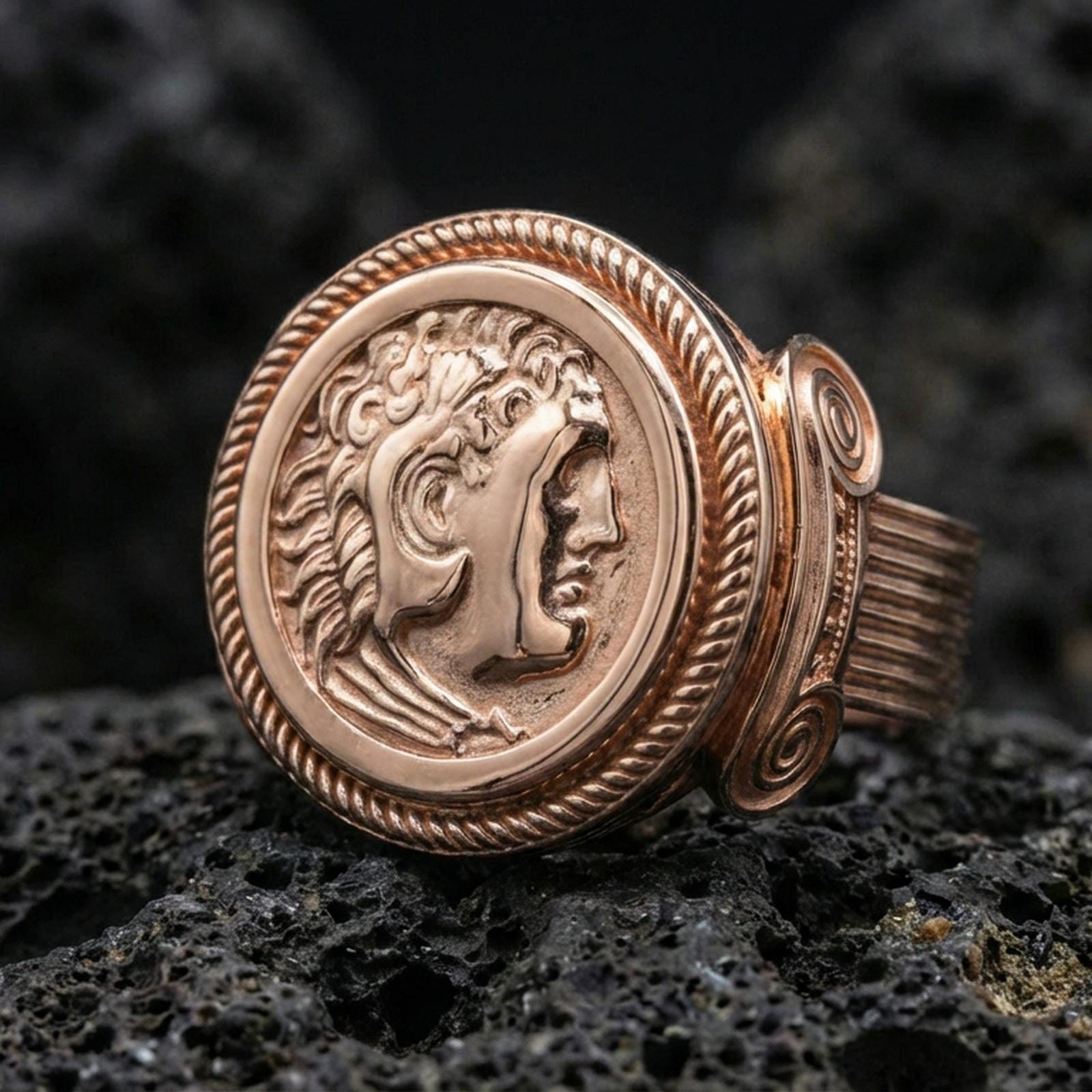 Rose gold plated ancient coin ring with detailed classical portrait and rope border bezel, close-up on volcanic rock