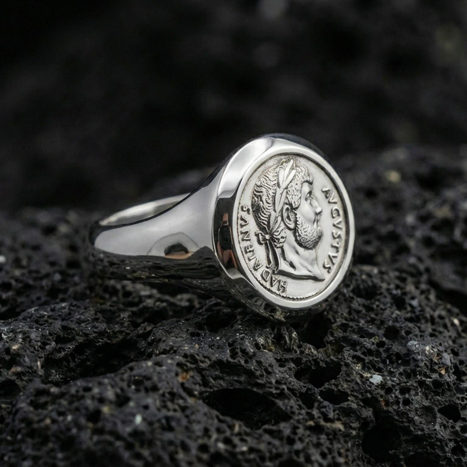 Polished silver ancient Roman coin signet ring with Augustus portrait relief and engraved Latin text, close-up on volcanic stone