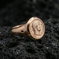 Load image into Gallery viewer, Rose gold plated ancient Roman coin ring with Augustus portrait and circular Latin lettering, close-up on volcanic rock
