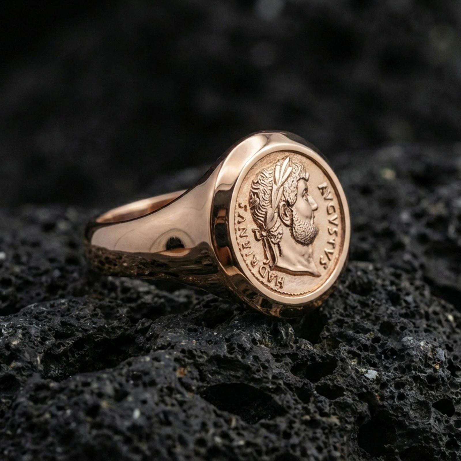 Rose gold plated ancient Roman coin ring with Augustus portrait and circular Latin lettering, close-up on volcanic rock