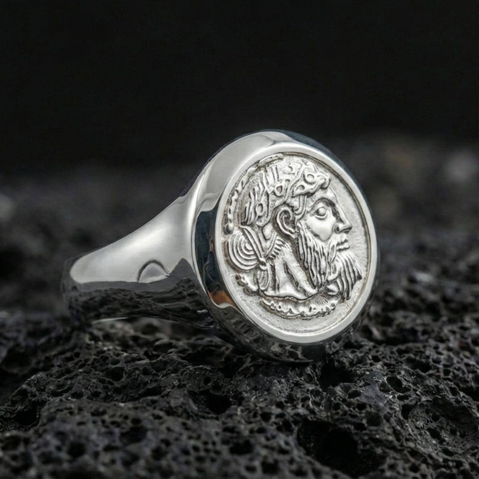 Polished silver coin portrait signet ring featuring a crowned bearded profile and raised round bezel, close-up on volcanic stone