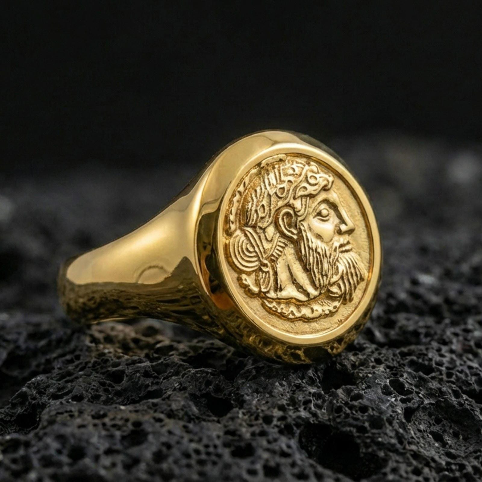 Gold plated ancient coin signet ring with detailed bearded king profile engraving, product-only macro on black volcanic rock