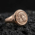 Load image into Gallery viewer, Rose gold plated coin portrait signet ring with crowned ruler relief and smooth tapered band, close-up on volcanic rock
