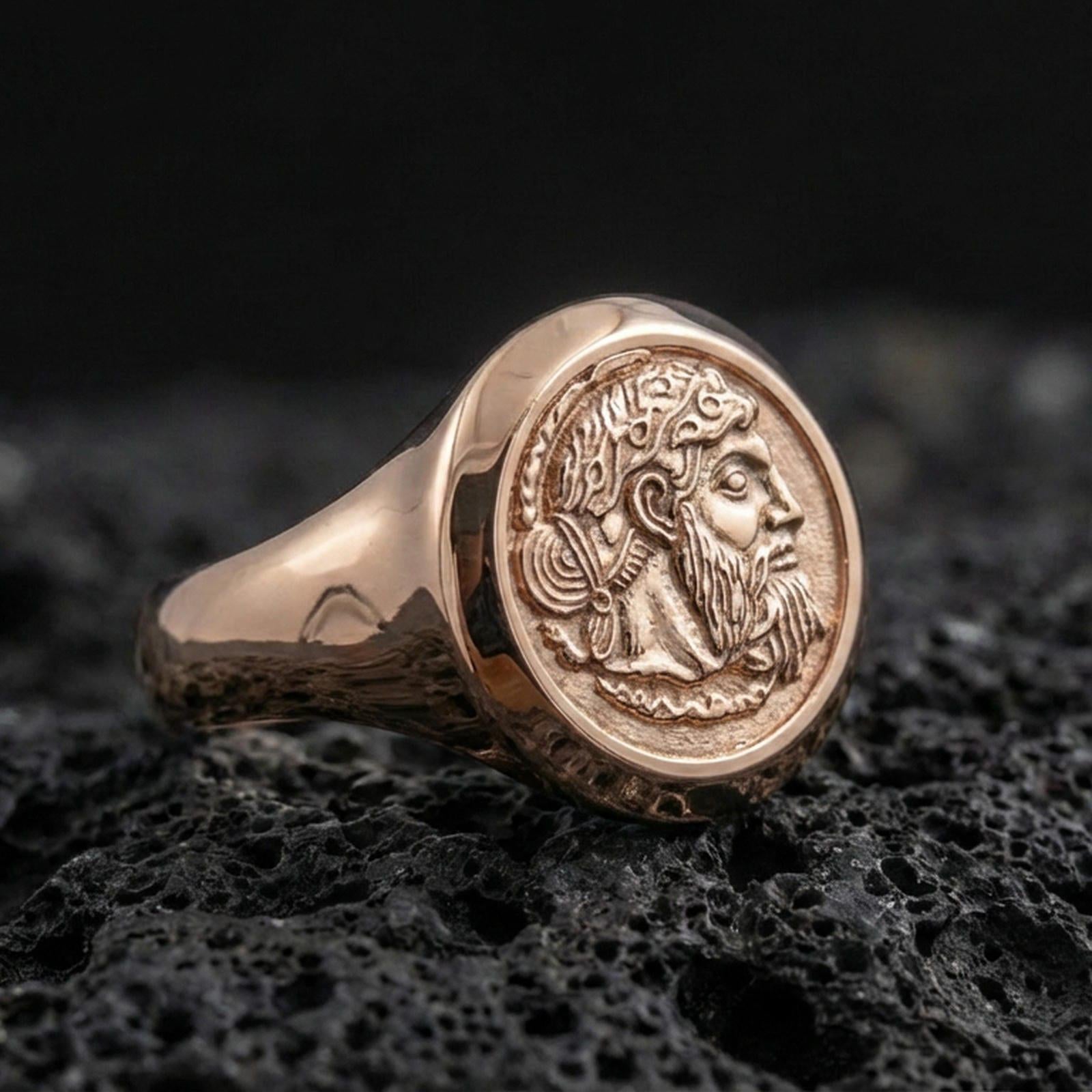 Rose gold plated coin portrait signet ring with crowned ruler relief and smooth tapered band, close-up on volcanic rock