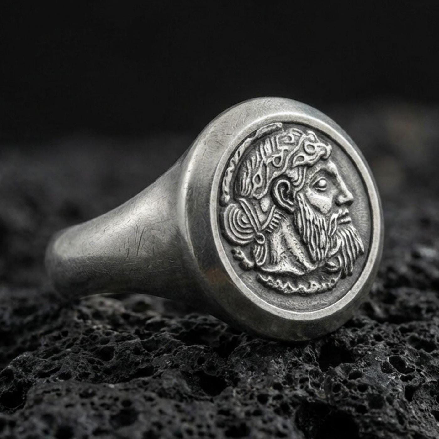 Oxidized sterling silver ancient coin signet ring with bearded ruler portrait relief, macro photo on black volcanic rock