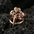 Load image into Gallery viewer, Rose gold plated heart dagger ring showing three hearts and an elongated dagger point, close-up on volcanic rock
