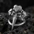 Load image into Gallery viewer, Oxidized sterling silver heart dagger ring with triple heart accents and pointed blade detail, macro photo on black volcanic rock

