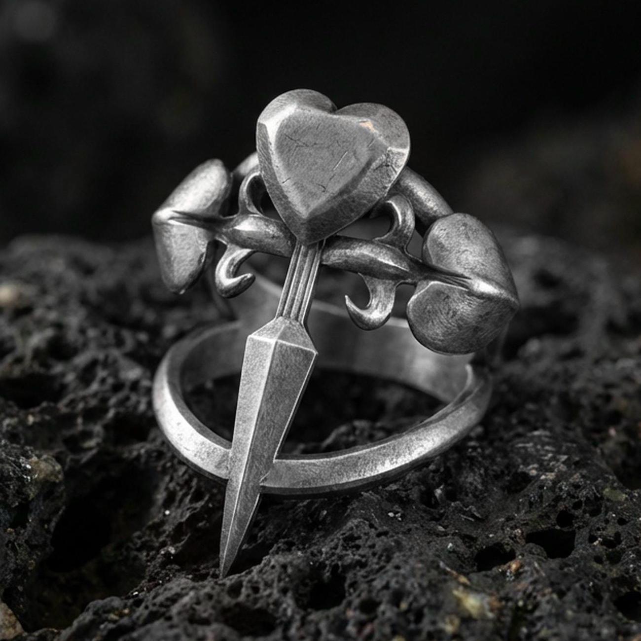 Oxidized sterling silver heart dagger ring with triple heart accents and pointed blade detail, macro photo on black volcanic rock