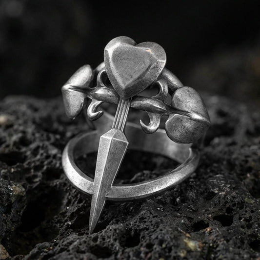 Oxidized sterling silver heart dagger ring with triple heart accents and pointed blade detail, macro photo on black volcanic rock