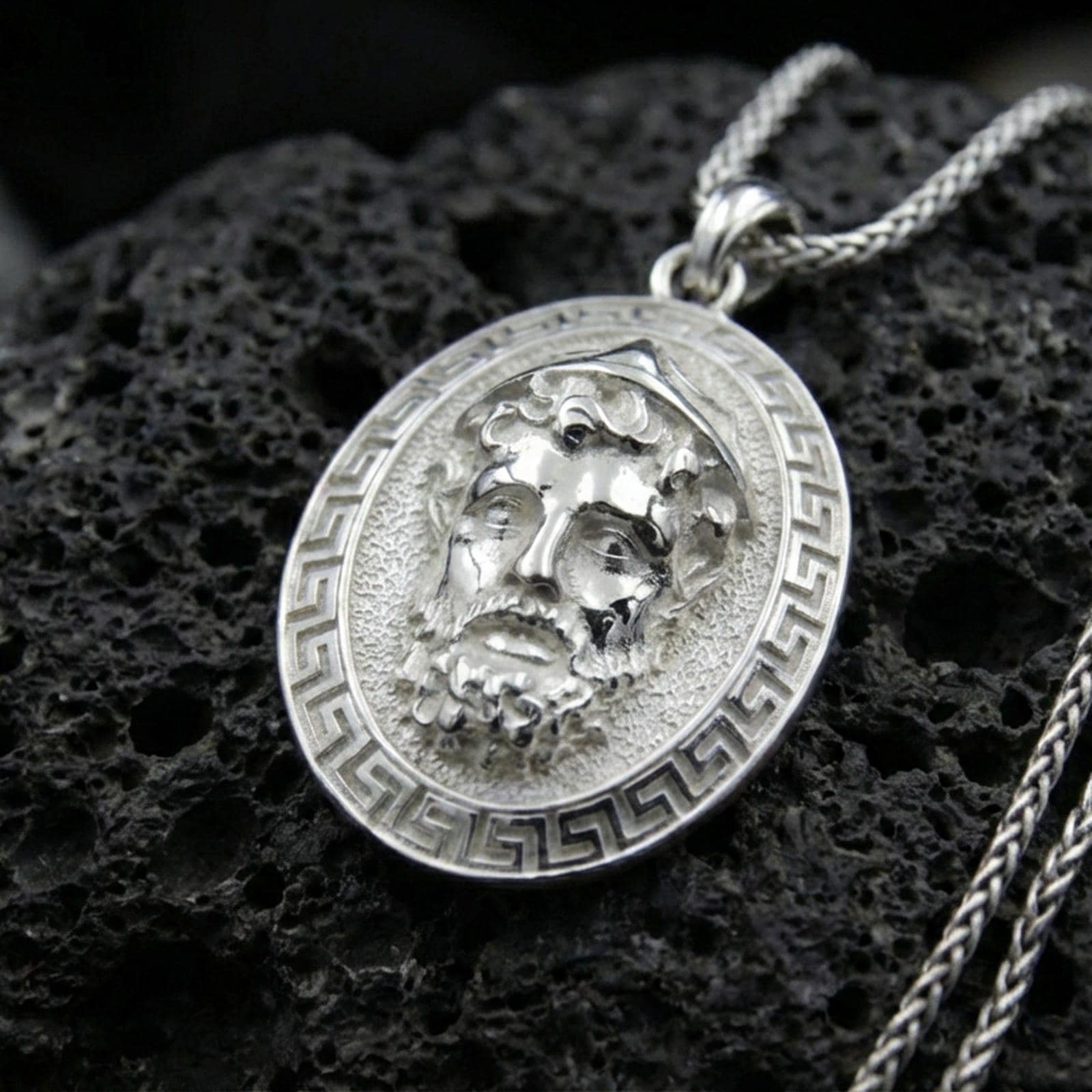 Polished silver Medusa medallion necklace on volcanic rock, crisp relief portrait and meander frame detail, close-up