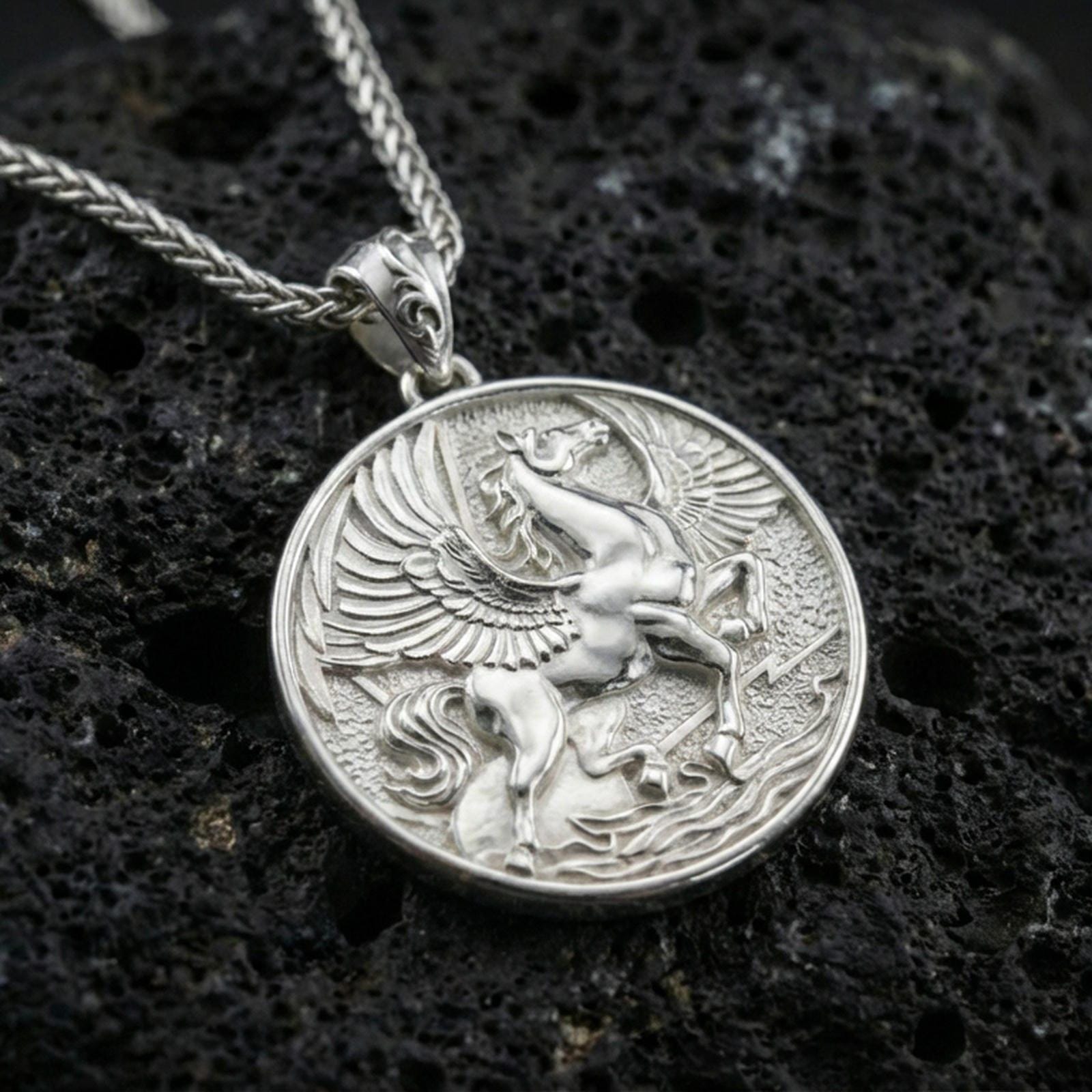 Polished silver winged Pegasus pendant on volcanic rock, crisp feather and musculature detail, close-up studio lighting